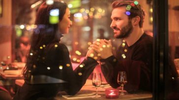A young couple of a man and a woman dressed in black while holding hands romantically the table romantic restaurant
