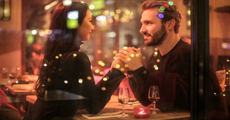 A young couple of a man and a woman dressed in black while holding hands romantically the table romantic restaurant