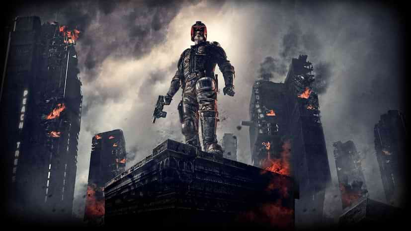 Judge Dredd movie wallpaper Jude Dredd wearing black uniform and red helmet and holding a gun while standing on a building roof in a burning city