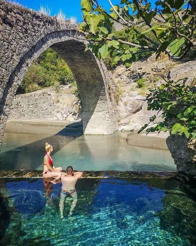 Man and woman relaxing in thermal bath in benja next to a stone bridge