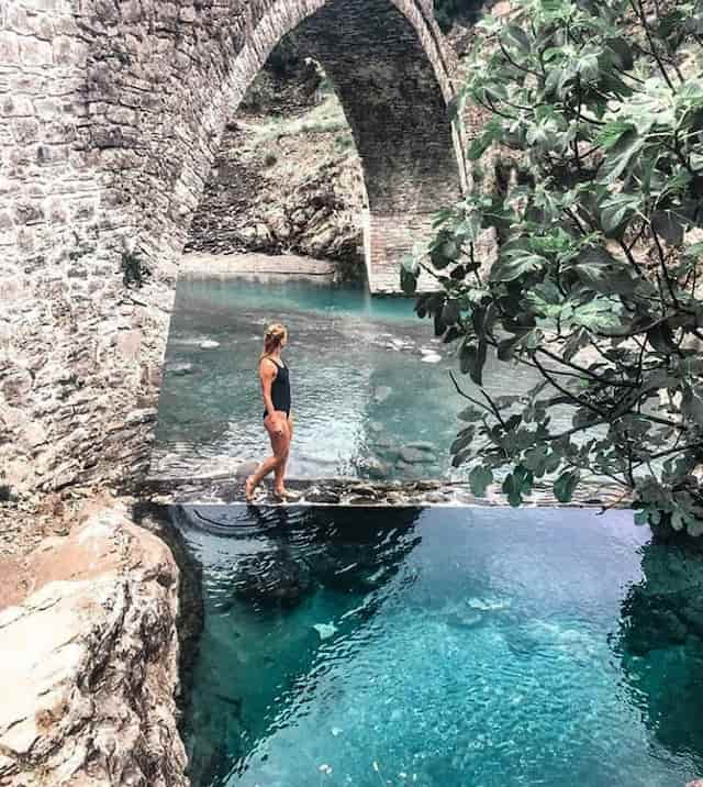 woman in black bathsuit relaxing in thermal bath in benja next to a stone bridge