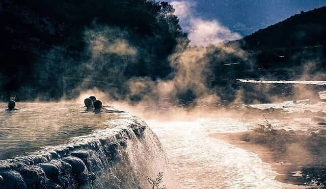 people swimming relaxing thermal bath of benja next to river steam on water