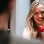 Blonde smiling girl flirting with a man on table while holding a red rose