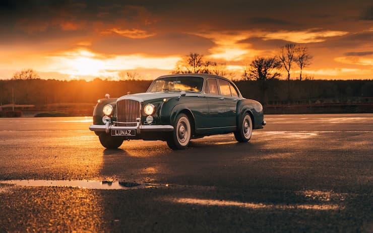 Bentley S2 1962 front facing lights on grey greenish metallic color in dusk background, electric Lunaz