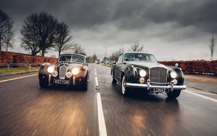 Bentley coupe and four-door Flying Spur front view on the road, cloudy skies, lights on, black and grey color, electrified Lunaz