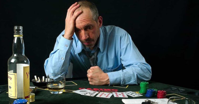 Sad and stressed man in blue shirt gambling and drinking alcohol
