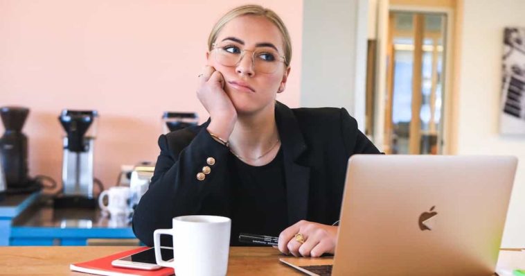 Sad blonde woman dressed in black is sitting in front of a silver macbook air