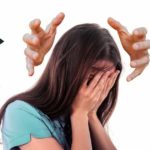 Brunette woman in a teal T-shirt covering her face anxiously