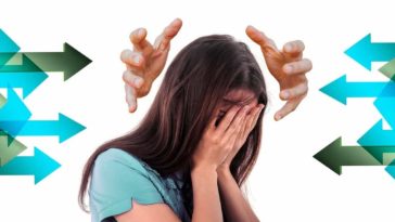 Brunette woman in a teal T-shirt covering her face anxiously