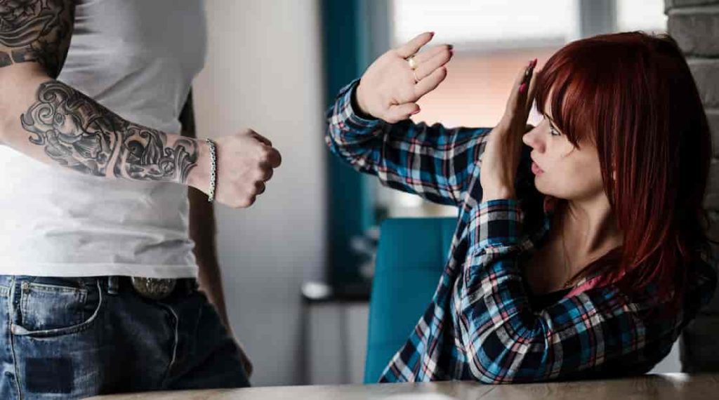 a tattooed man preparing his fist to punch a redhead woman