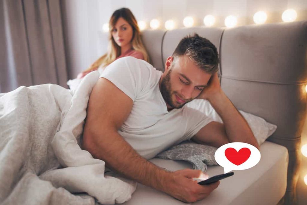 man in bed texting to another woman while his wife is watching