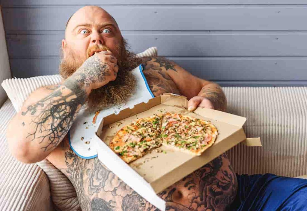 glutonous bearded man with a belly eating pizza on the couch