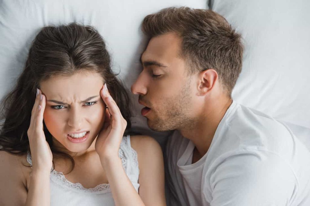 woman having a headache next to her partner in bed