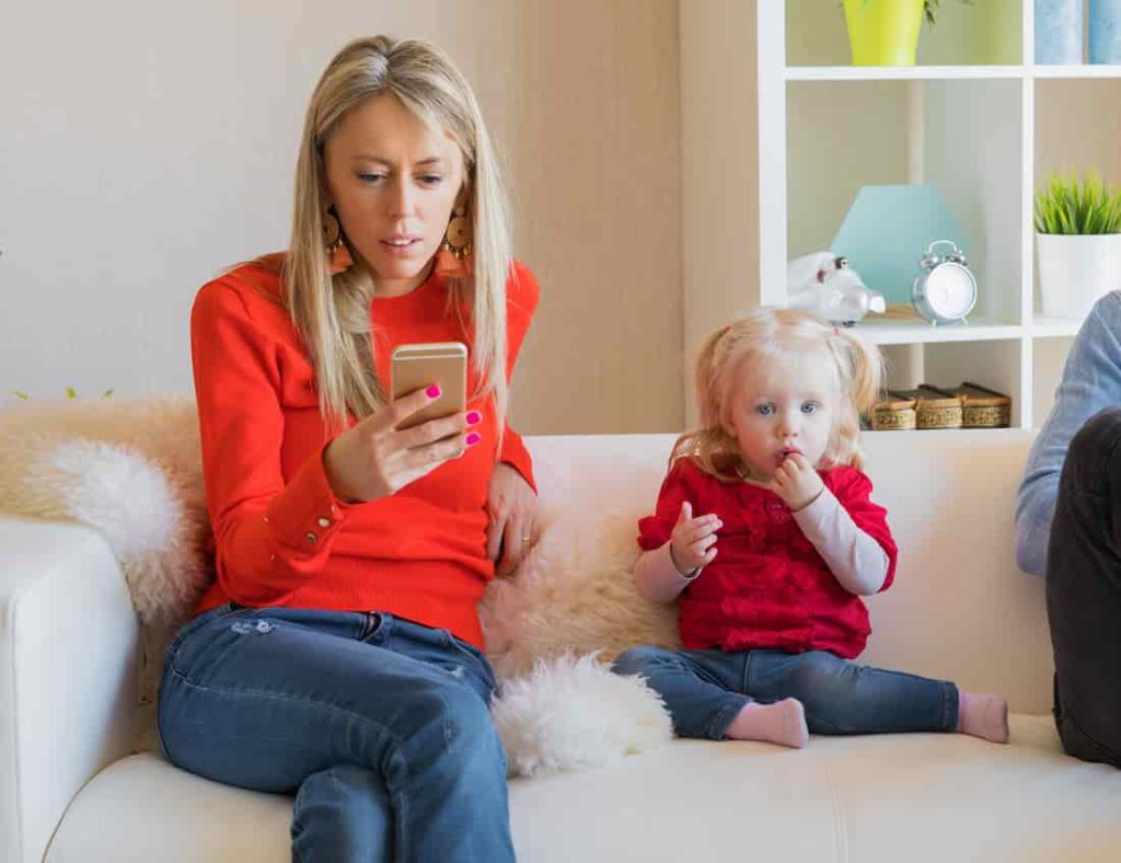 woman in red blazer looks at phone and ignores her daughter