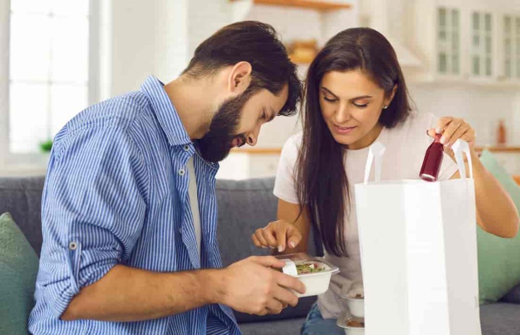 a couple sitting on the couch and eating takeout food