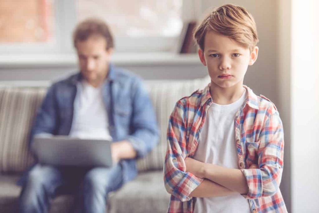 father sits on couch on his laptop and ignores son