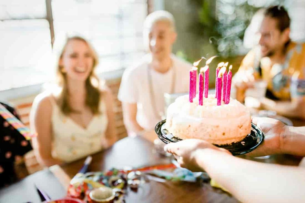 four people celebrating birthday with a cake and pink canddles