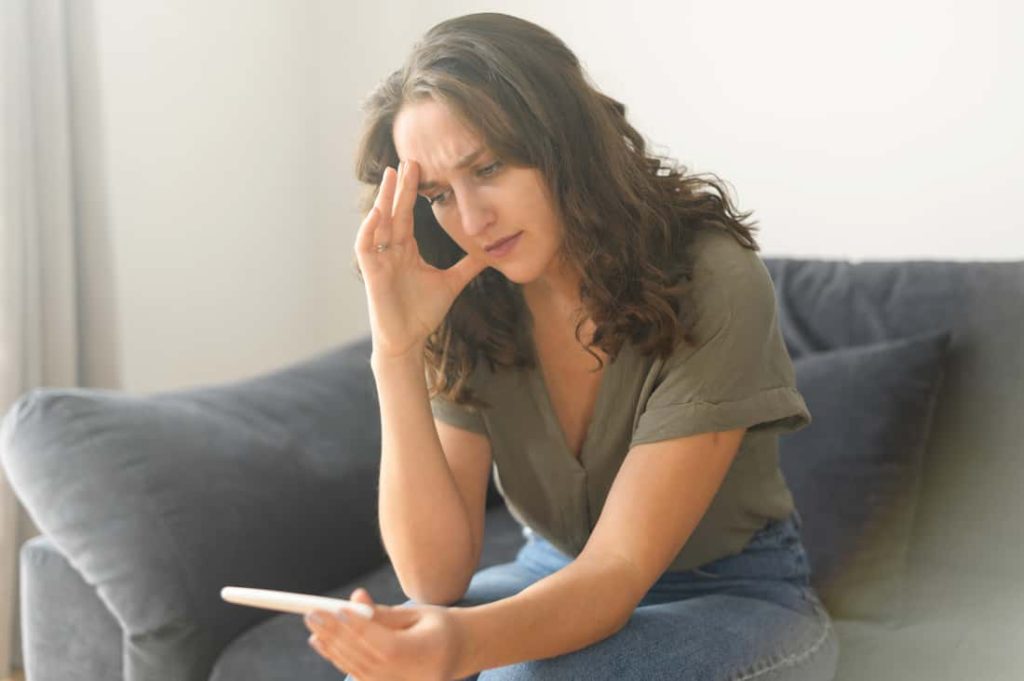 woman sitting on couch and looking concerned at pregnacy test